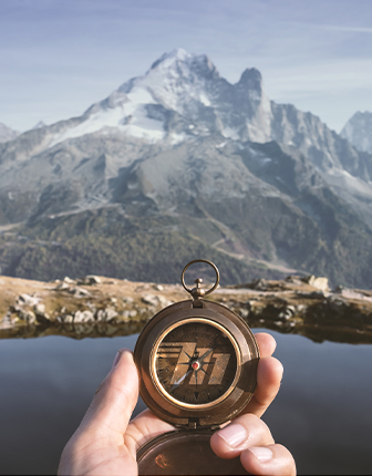 hand holding compass with mountains in background